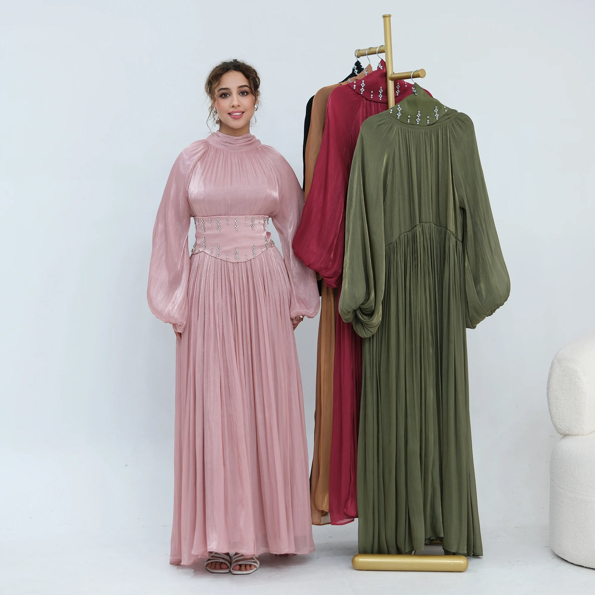 Une femme modélise une abaya rose fluide avec une ceinture ornée, à côté de deux tenues similaires.