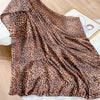 A brown leopard print silk satin scarf draped on a white surface.
