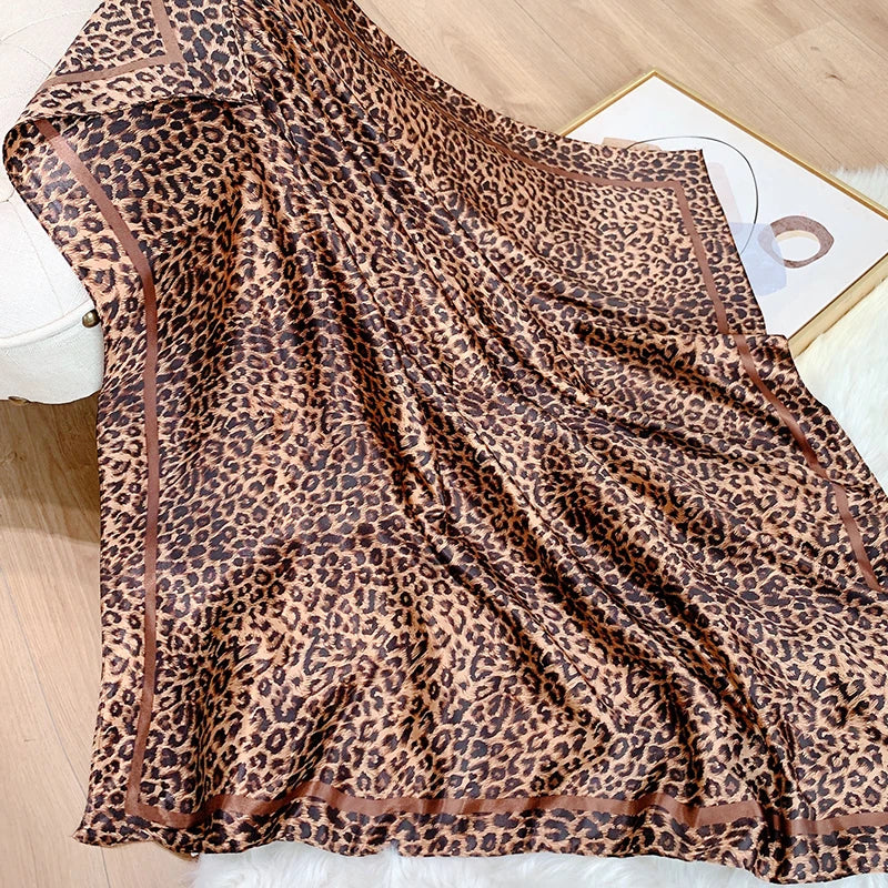 A brown leopard print silk satin scarf draped on a white surface.