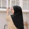 Une femme portant un hijab noir et un haut beige se tient devant des armoires blanches.
