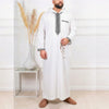A man wearing a white Moroccan embroidered thobe jellaba with black detailing and a bracelet.