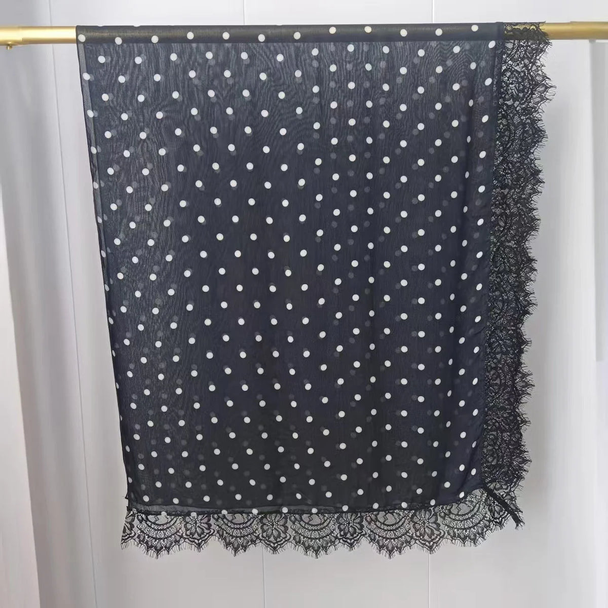 Hijab de tela transparente gris oscuro con lunares blancos y ribete de encaje colgado en una barra.