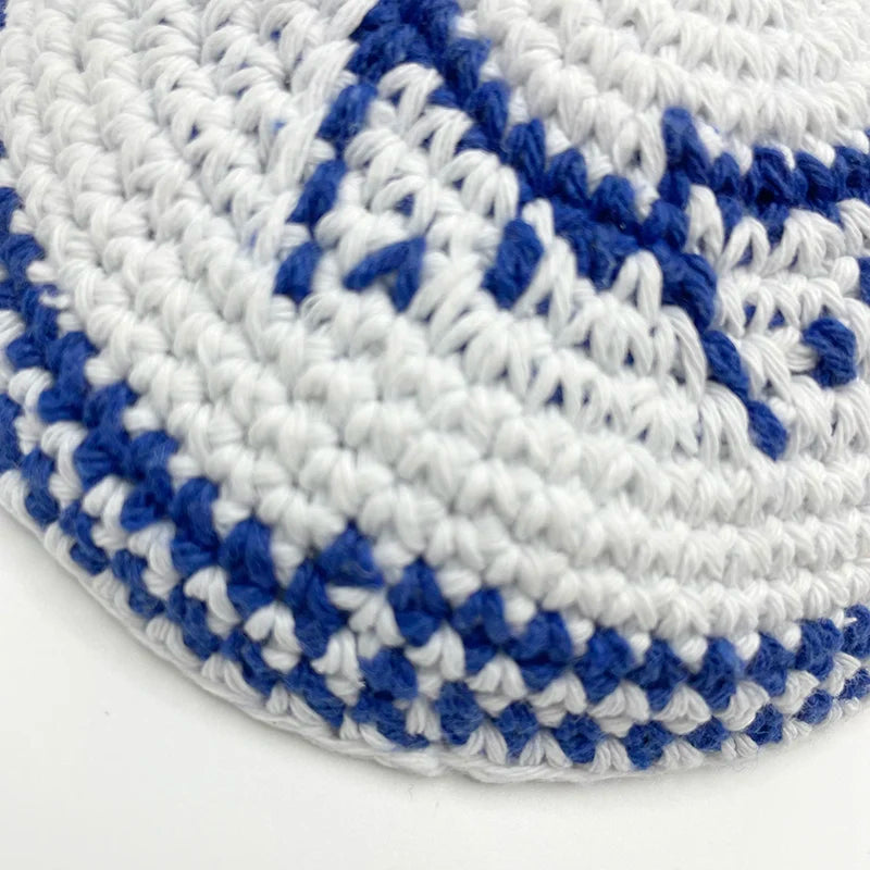 Gros plan d'une kippah ou yarmulke tricotée à la main juive, avec des motifs géométriques blancs et bleu royal.