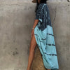 Eine Frau in einem tie-dye Kimono-Überkleid und einem Strohhut steht vor einer strukturierten Wand.