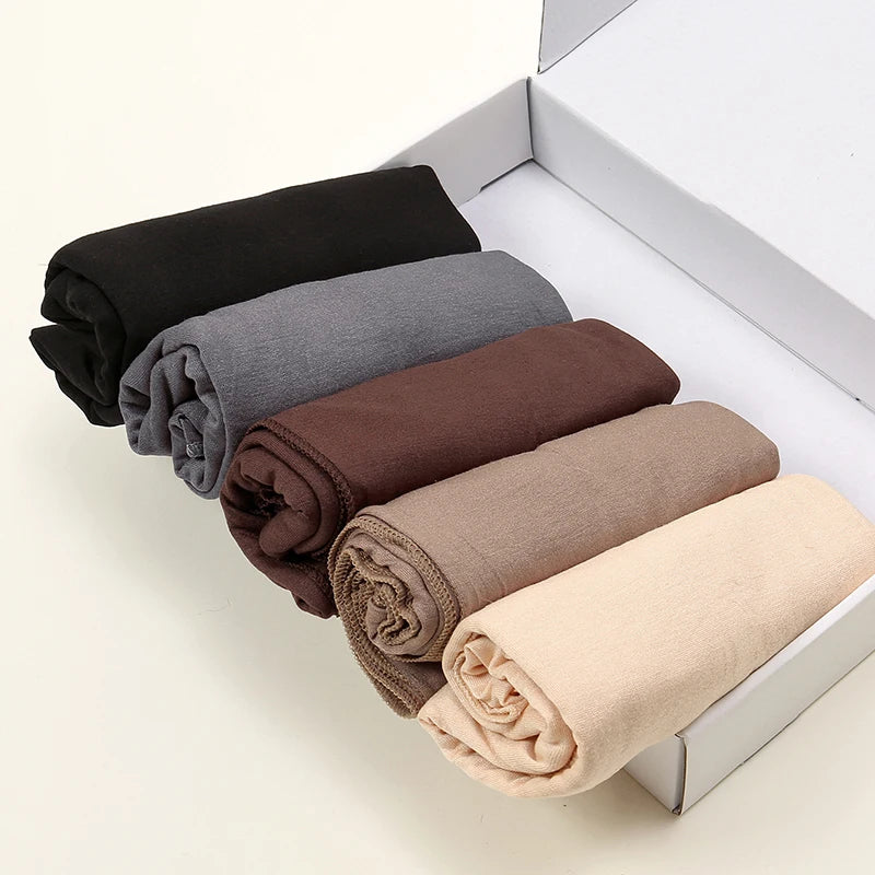 Une boîte contenant plusieurs foulards de hijab solides roulés dans les couleurs noir, gris, marron et beige.