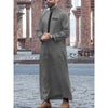 A man wearing a grey embroidered thobe long-sleeve Islamic jubbah standing outdoors.