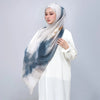 Eine Frau trägt einen Aquarelldruck-Leinen-Baustoff-Hijab-Schal in Blau und Weiß vor einem hellgrauen Hintergrund.