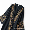 A black abaya featuring intricate gold floral embroidery on the sleeves and front panel.