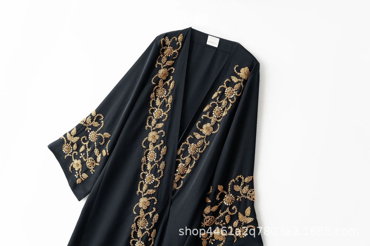 A black abaya featuring intricate gold floral embroidery on the sleeves and front panel.