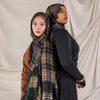A woman wearing a plaid hijab scarf over a black top, standing against a light background.