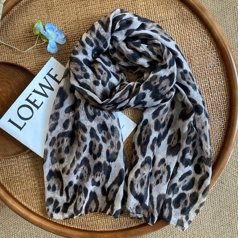 Écharpe pashmina imprimée léopard marron foncé et noir drapée sur une assiette en bois avec une étiquette blanche.