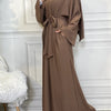 A woman wearing a long, flowing brown abaya or kaftan with a tied waist detail.