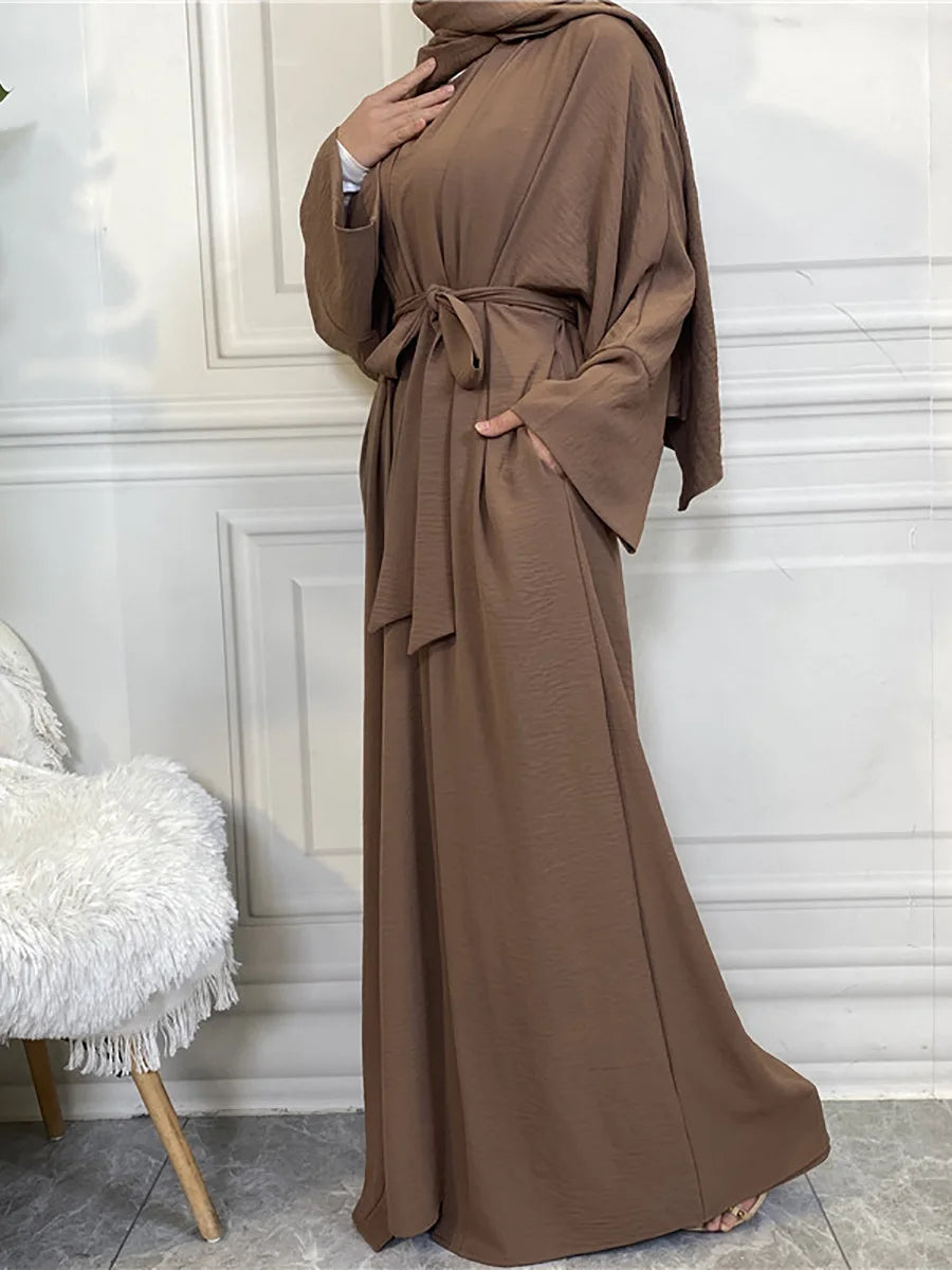 A woman wearing a long, flowing brown abaya or kaftan with a tied waist detail.