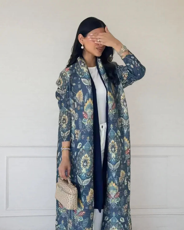 A woman wearing a blue floral patterned abaya cardigan coat with a black inner layer and white pants.