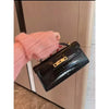 A hand is holding a black crocodile pattern shoulder bag against a light wood background.