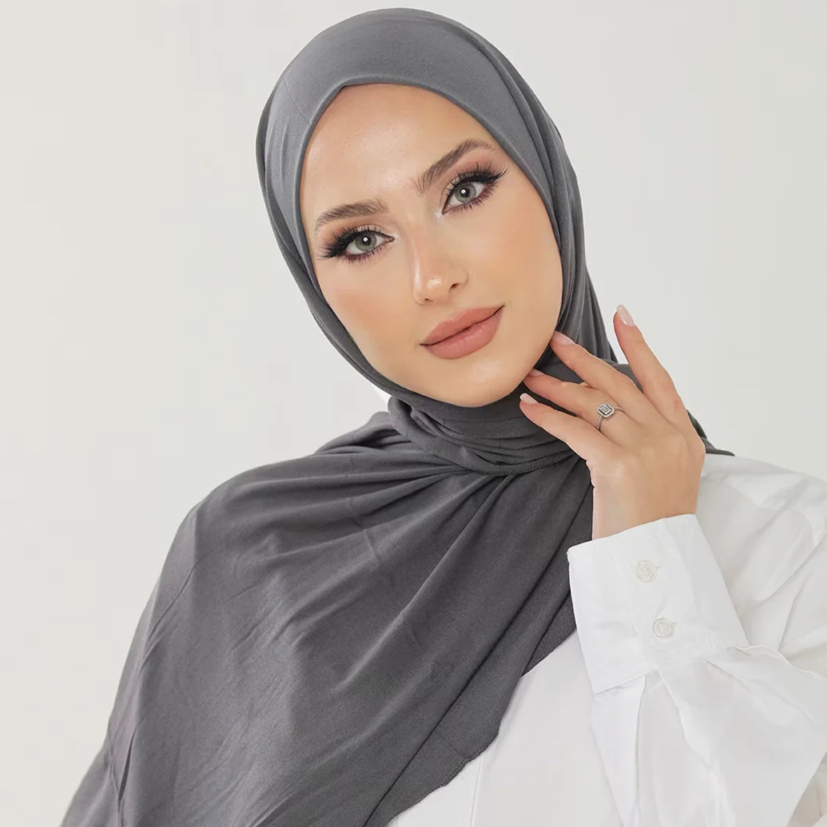 Una mujer vistiendo un pañuelo de hijab de algodón premium gris y elástica con una camisa blanca.