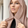 Eine Frau trägt einen beigen Instant-Chiffon-Hijab mit einer Kappe und blickt direkt in die Kamera.