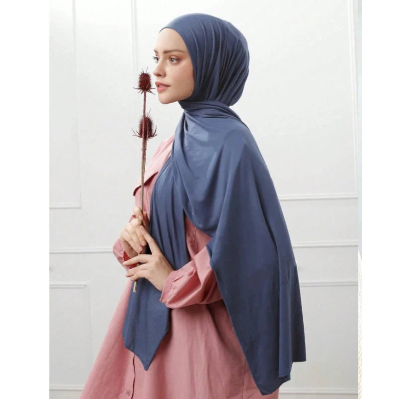 Eine Frau trägt einen blauen Strickschal als Kopftuch über ein rosa Kleidungsstück und hält eine getrocknete Blume.