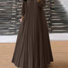 Une femme portant une longue caftan marron plissé à bordure noire et un hijab foncé.