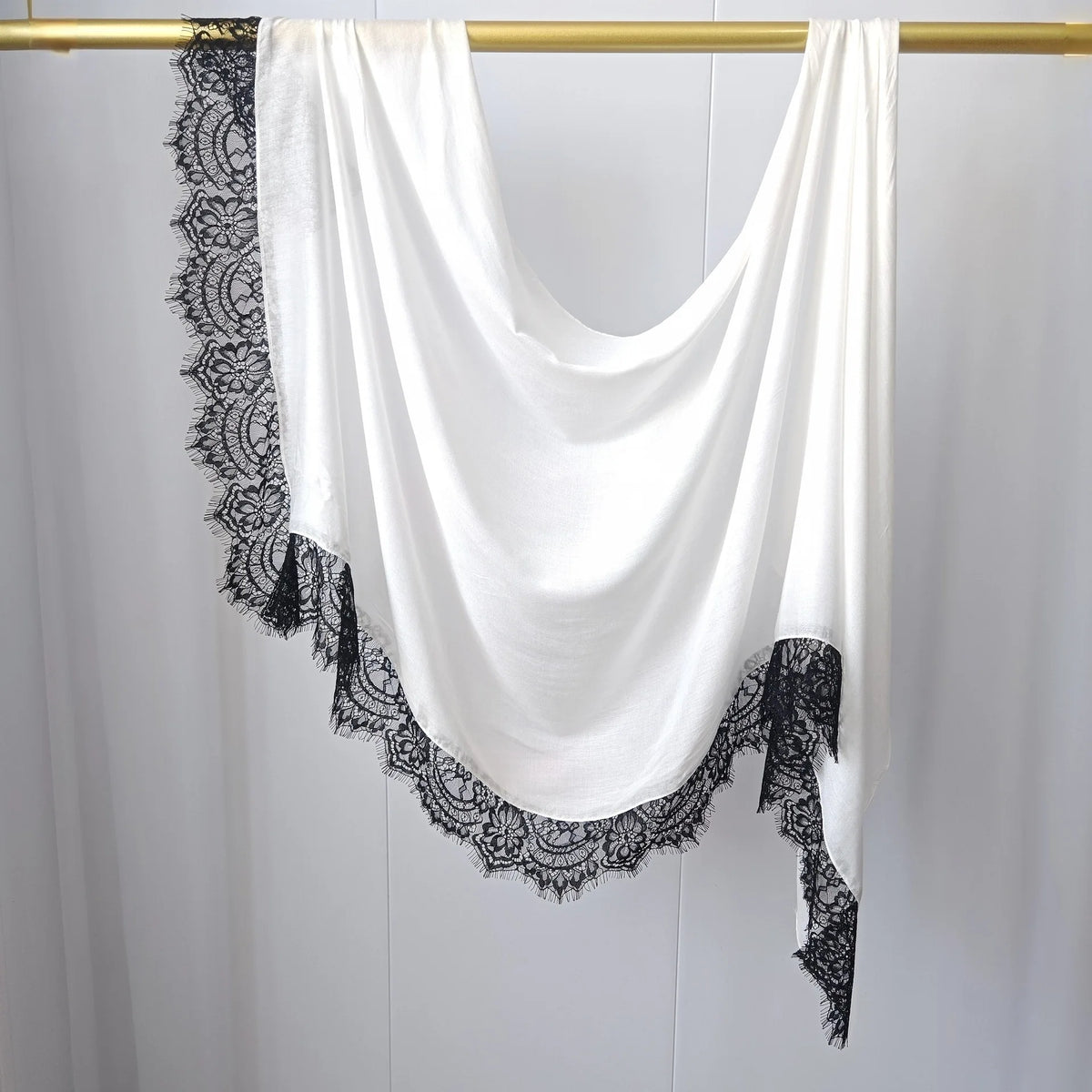 Hijab de malla blanca con estampado doble, drapeado sobre un perchero dorado.