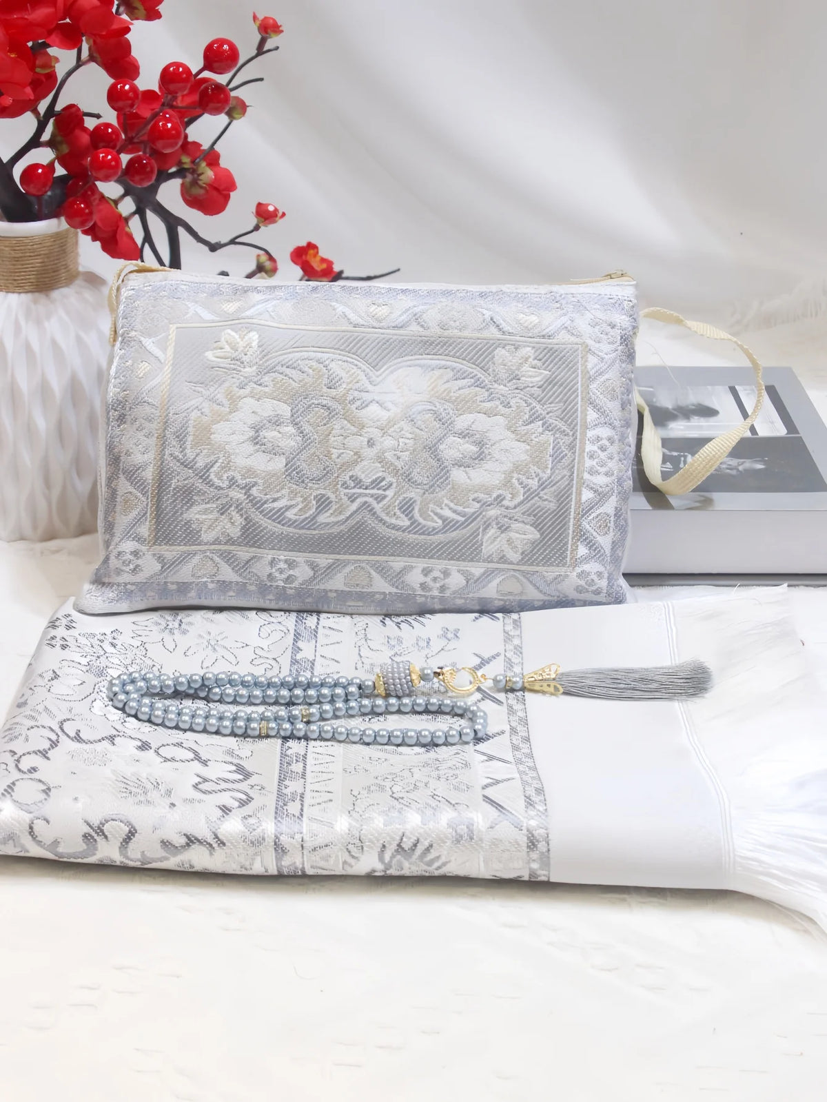 Ein Set muslimischer Gebetsmatte mit Perlenstickereien und einer tragbaren Stofftasche auf weißem Untergrund.