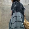 Rückansicht einer Frau in einem hellblauen Tie-Dye Kimono-Überkleid und einer breiten Strohtasche vor einer grauen Wand.
