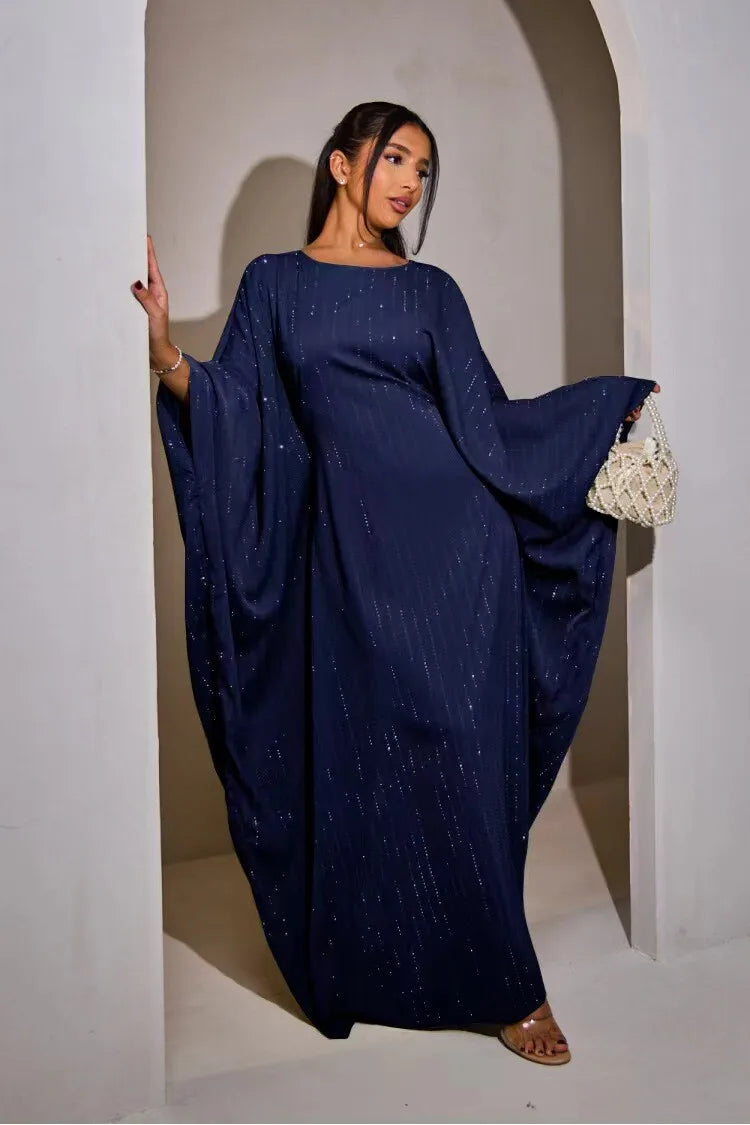 Modelo vistiendo una abaya de manga de murciélago azul marino de lujo para noche, de pie en un arco blanco.