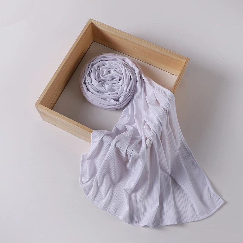 A white ribbed jersey hijab scarf is rolled and draped within a light wooden frame.