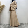 Eine Frau trägt eine elegante beige Maxi-Abaya mit blauen Akzenten vor einer weißen Wand.