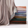 A stack of folded, watercolor-printed modal scarves in various muted tones of pink, purple, blue, and green.