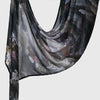 A dark gray sheer linen hijab scarf with an elegant floral and abstract print draped over a surface.