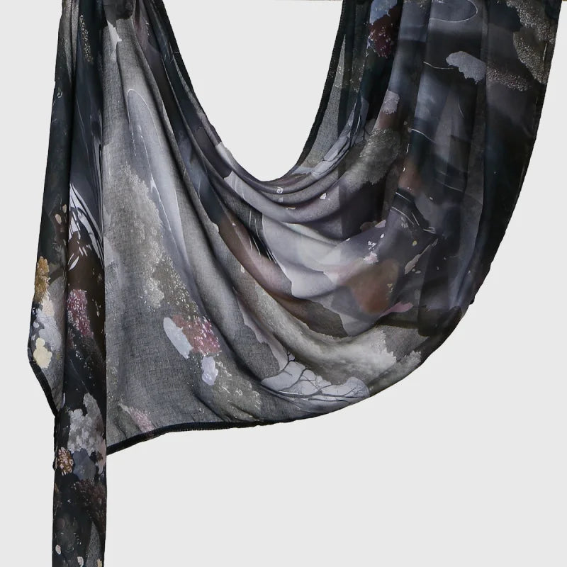 A dark gray sheer linen hijab scarf with an elegant floral and abstract print draped over a surface.
