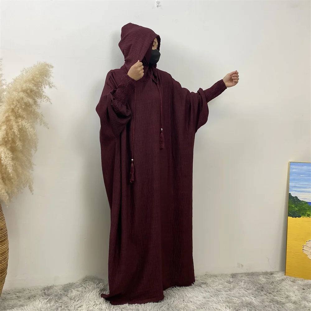 Une abaya marron avec capuche et manches batwing, exposée contre un mur blanc.