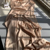 Fließender, hellbeiger Crinkle-Satin-Chiffon-Hijab, drapiert auf einer Oberfläche mit Schatten.