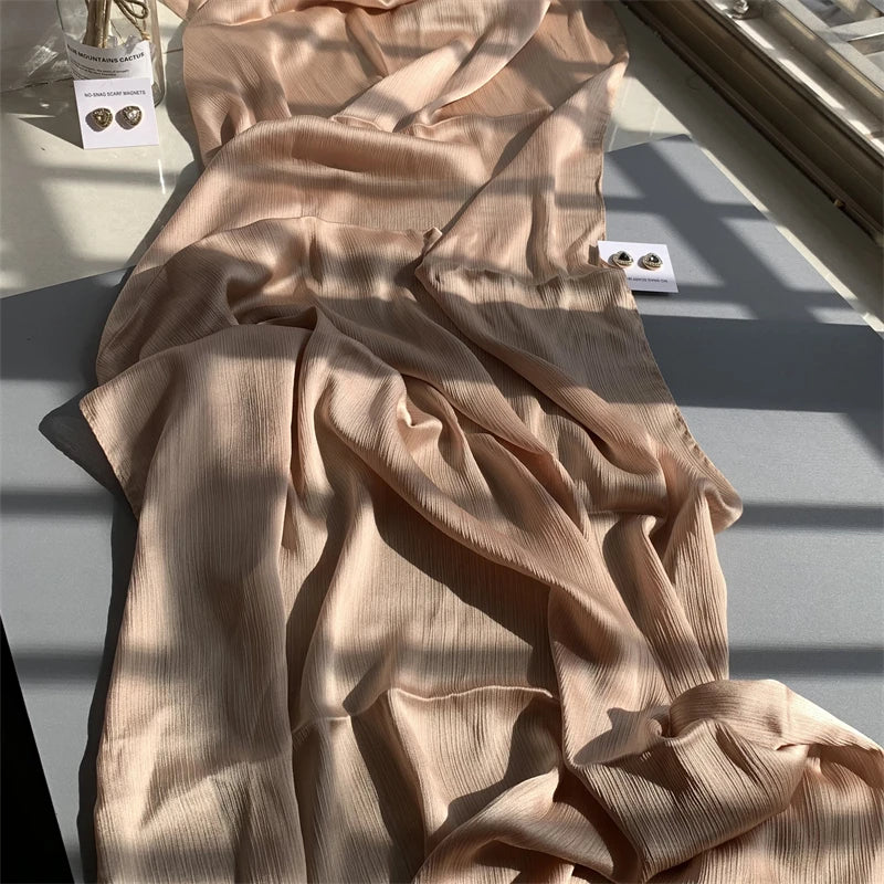 Fließender, hellbeiger Crinkle-Satin-Chiffon-Hijab, drapiert auf einer Oberfläche mit Schatten.