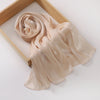 Un châle en mousseline crinklée beige clair et scintillant drapé dans un cadre en bois.