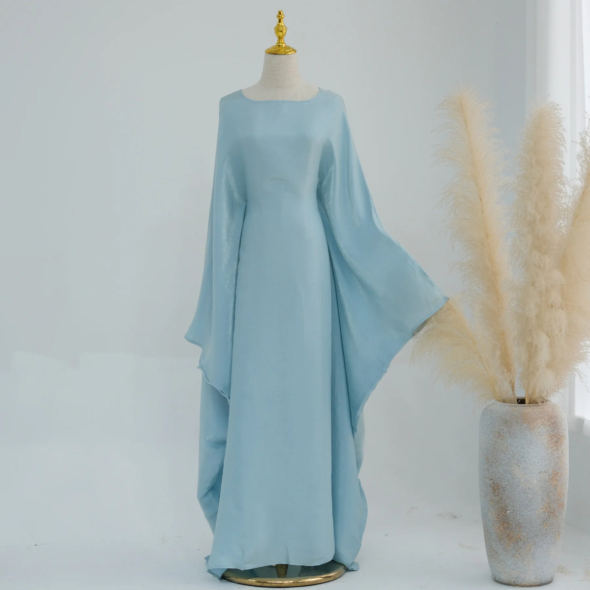 Elegantes hellblaues Kaftan-Kleid auf einem Mannequin neben getrockneten Ziergräsern.