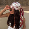 A woman wearing an elegant silk dot print scarf tied around her hair, looking to the side.