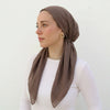 A woman wearing a solid brown linen elastic headscarf cap and white top.