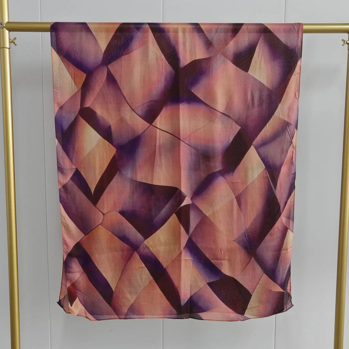 Quadratischer Schal mit geometrischem Muster in Violett- und Rosatönen auf hellem Stoff.