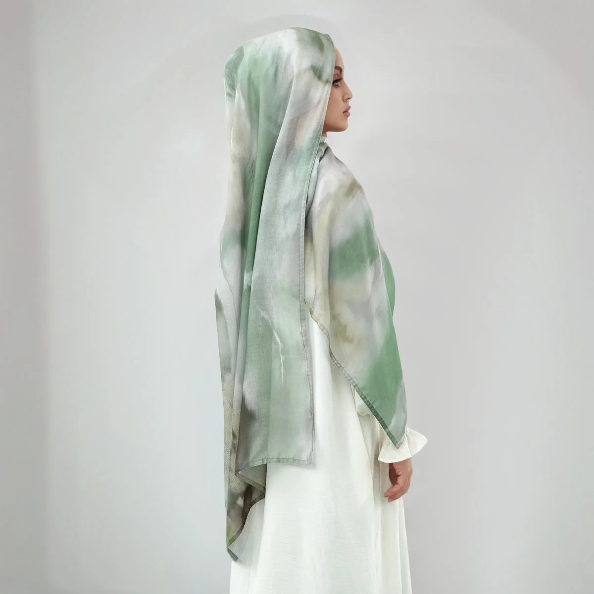 Eine Frau trägt einen Aquarelldruck-Baumwoll-Leinen-Hijabschal in Grüntönen und Grau.