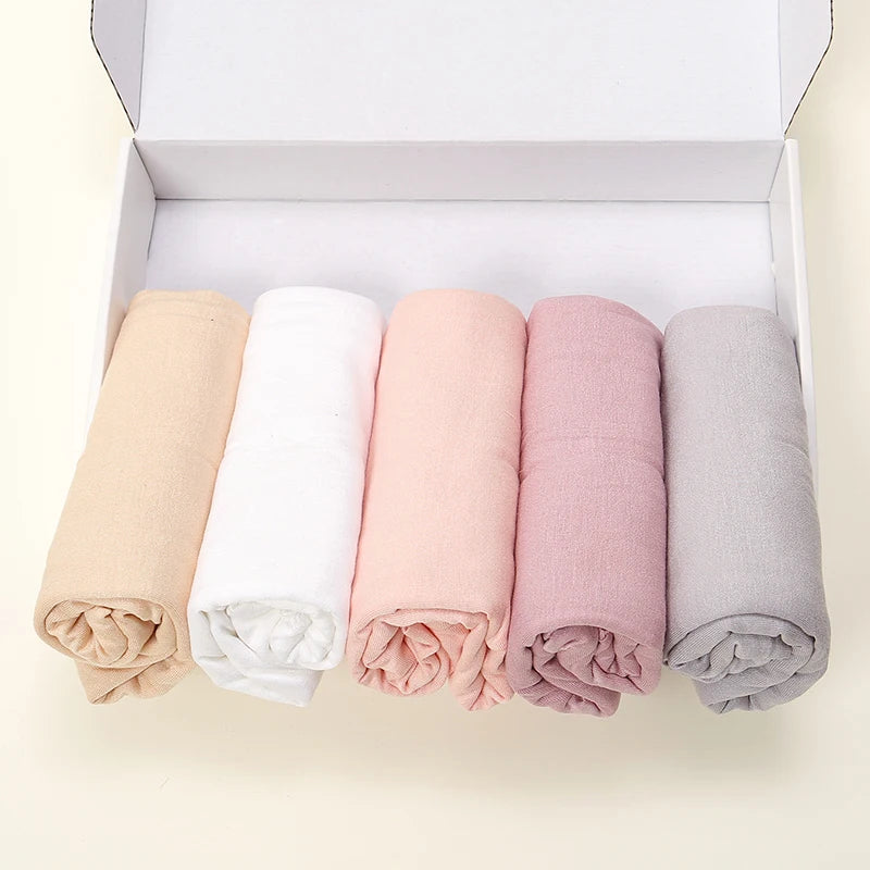 Une boîte contient cinq foulards de hijab unis roulés dans les couleurs beige, blanc, rose, mauve et gris.