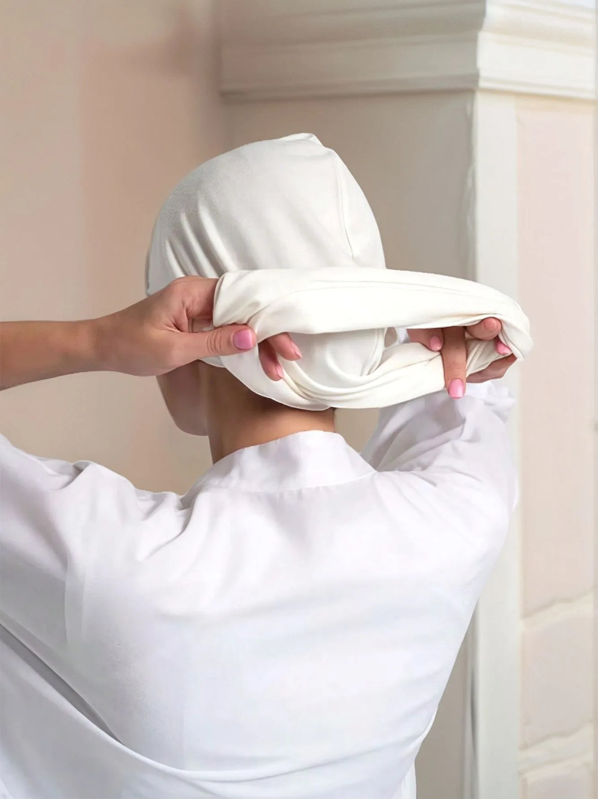Una persona ajustando un pañuelo instantáneo de algodón elástico blanco en su cabeza.