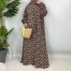 Una mujer vistiendo una elegante kaftan abaya floral con estampado blanco y negro, de pie contra un fondo gris claro.