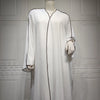 Vestido abaya blanco, largo y holgado, exhibido en maniquí contra una pared de paneles gris claro.