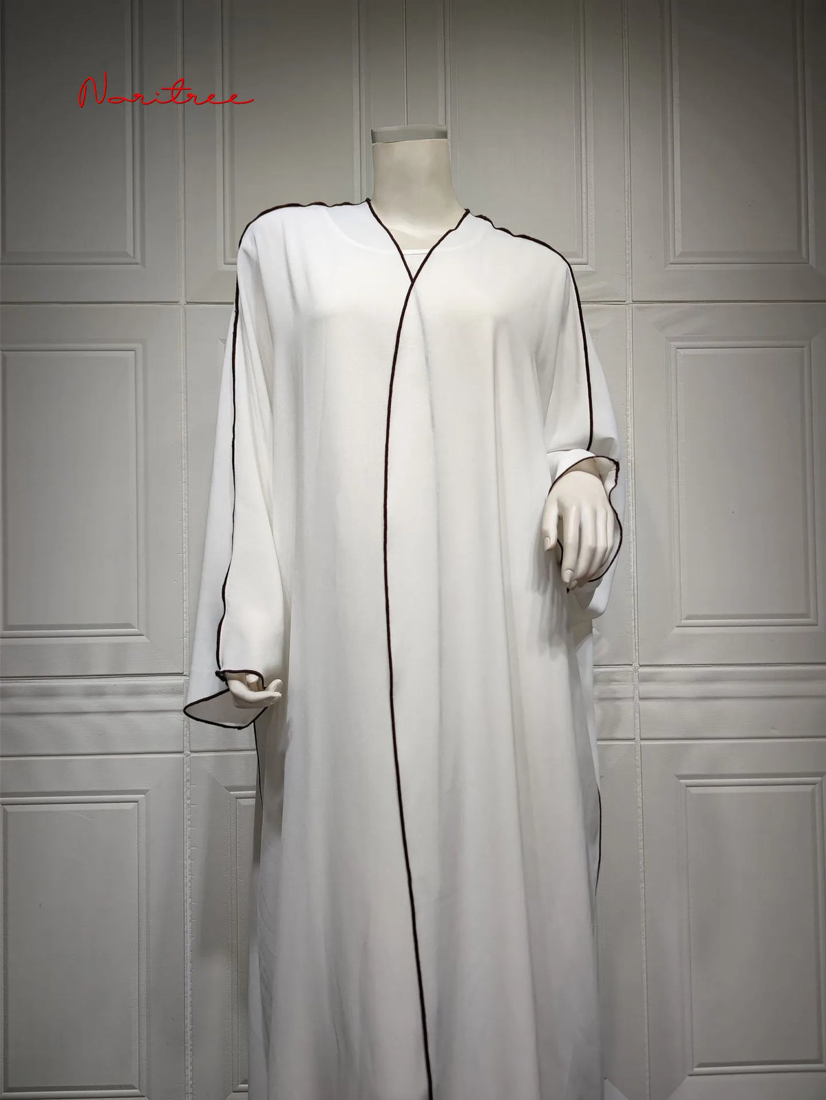 Vestido abaya blanco, largo y holgado, exhibido en maniquí contra una pared de paneles gris claro.