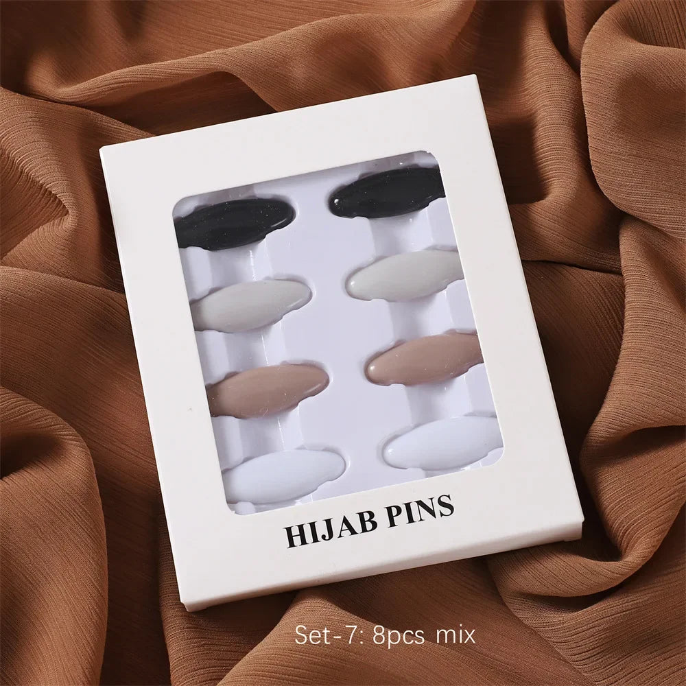Ein Set von sieben gemischten Hijab-Pins in verschiedenen Schattierungen von Schwarz, Grau und Beige in einer weißen Box.
