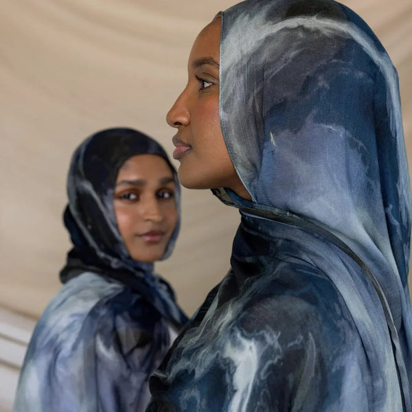 A close-up of two women wearing elegant printed voile hijabs looking at each other.