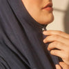 Close-up of a hand adjusting a navy blue hijab with a silver macaron brooch clip.