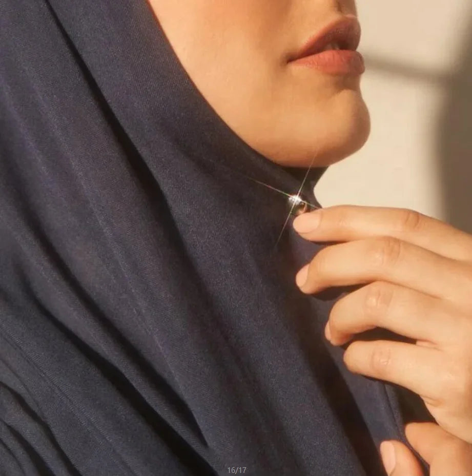 Close-up of a hand adjusting a navy blue hijab with a silver macaron brooch clip.